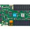 Green development board with numerous edge connectors and two labeled ports (PC and Display), plus a yellow battery pack on a red/black wire on the right side.